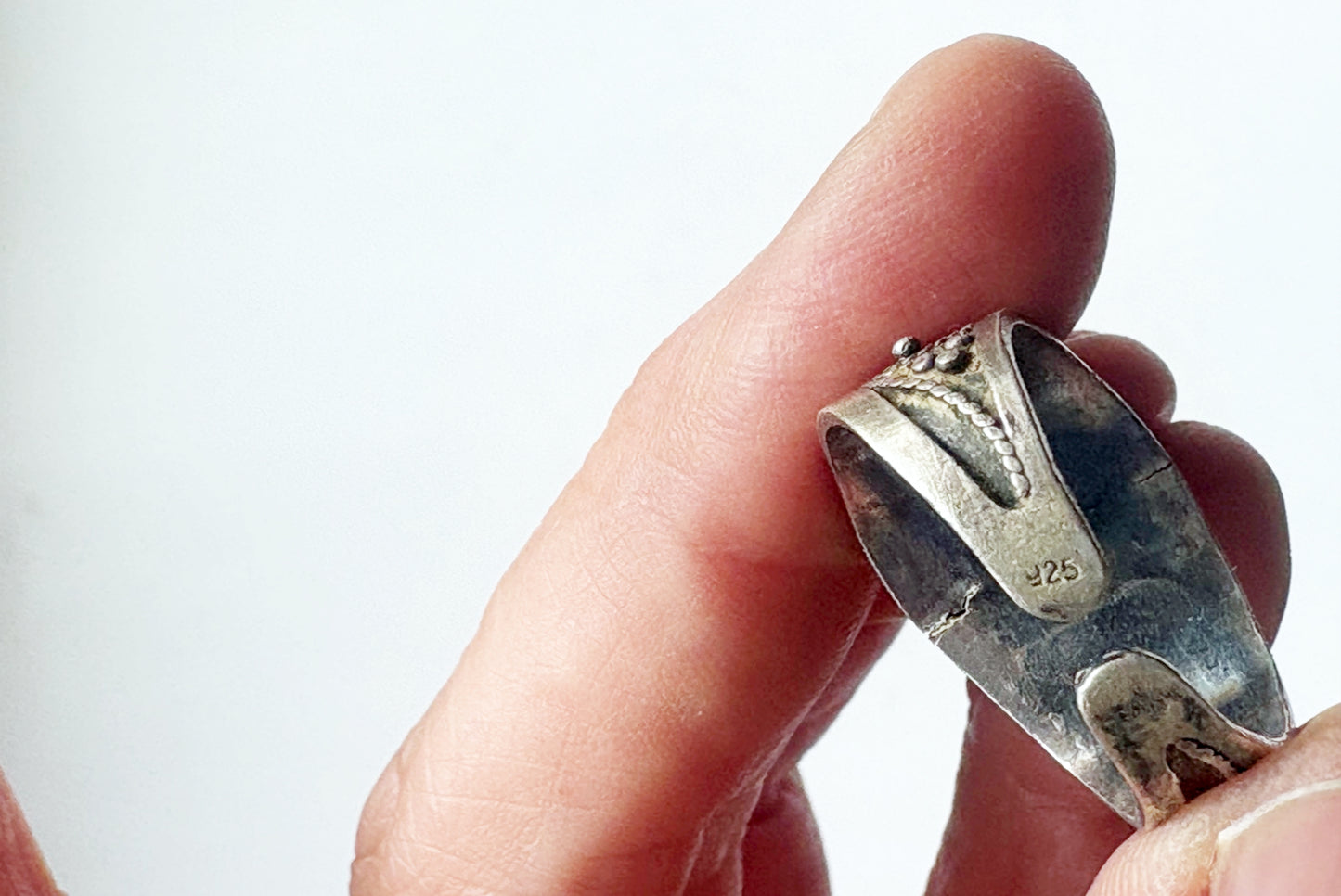 A close-up of a hand holding a silver ring with a textured, hammered finish and a visible '925' sterling silver hallmark on the inside.
