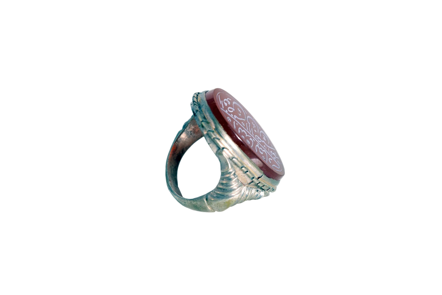 A vintage-style signet ring featuring a round reddish-brown carved stone with engravings, set on a weathered silver band, photographed on a plain white surface.
