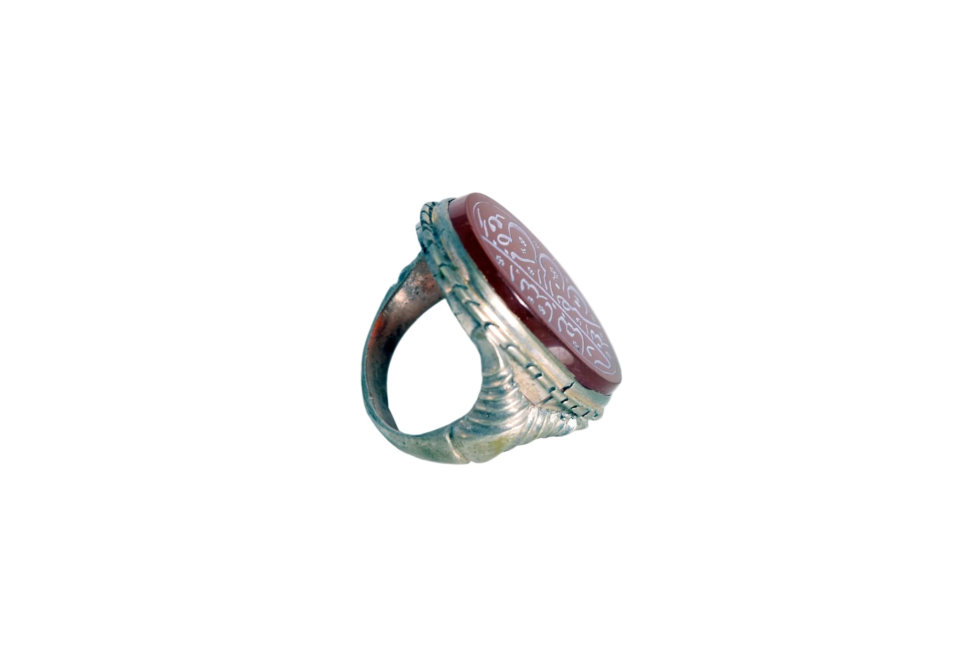 A vintage-style signet ring featuring a round reddish-brown carved stone with engravings, set on a weathered silver band, photographed on a plain white surface.