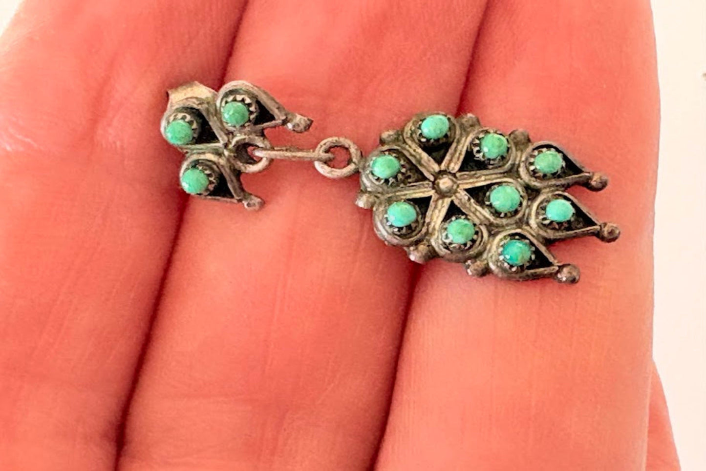 Silver earring with turquoise stones held between fingers on a hand