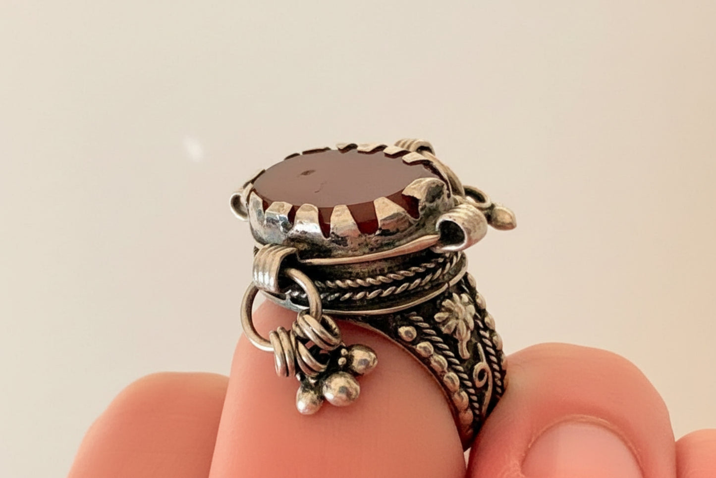 Silver ring with a brown stone on a hand against a beige background