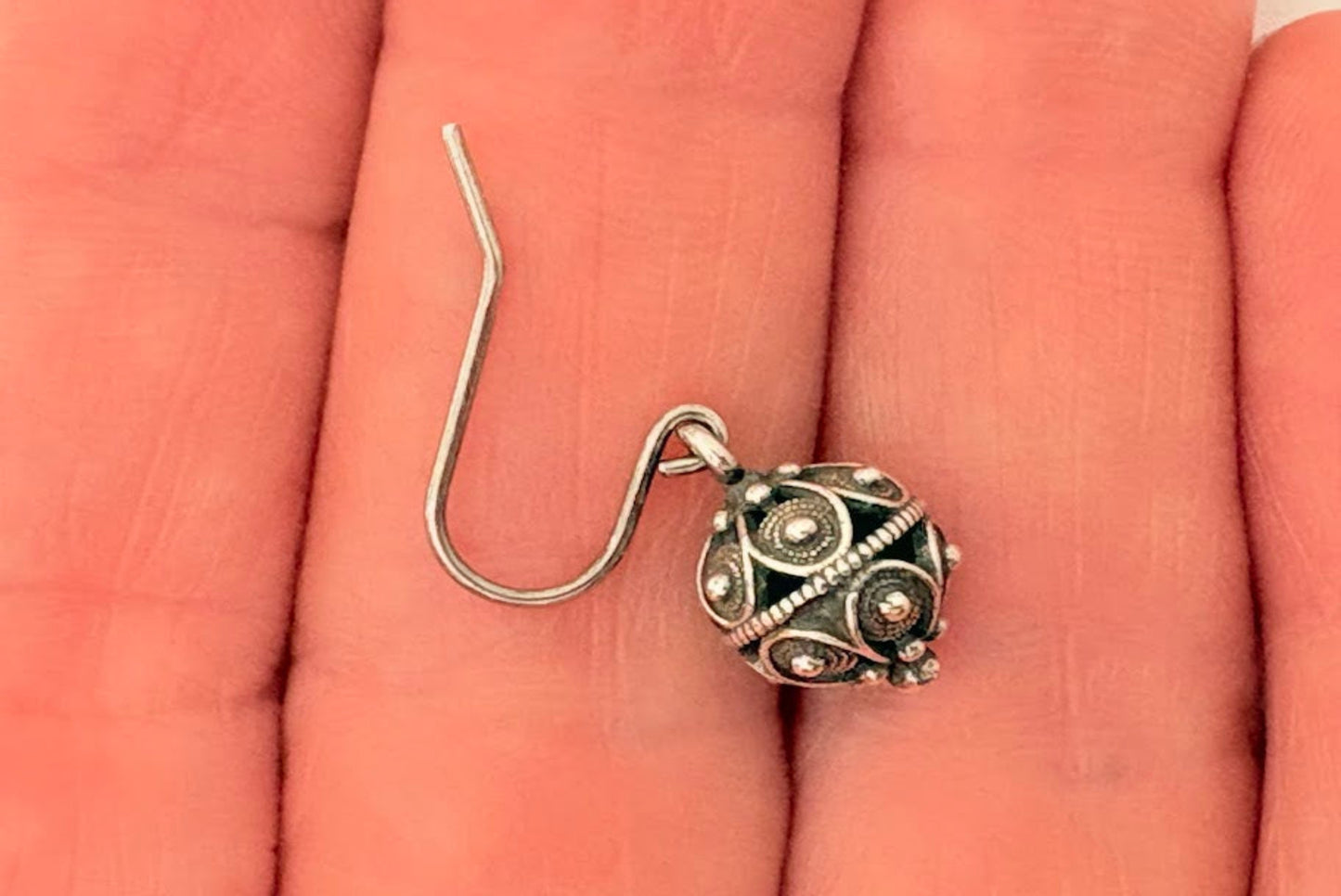 Silver earring with intricate design on a hand