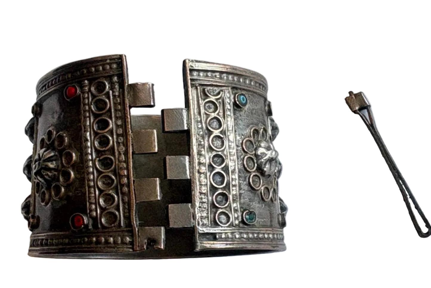 Ornate silver bracelet on a white surface with a pin closure on the side.