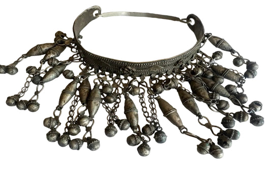 Decorative silver torc necklace with hanging beads on a light background