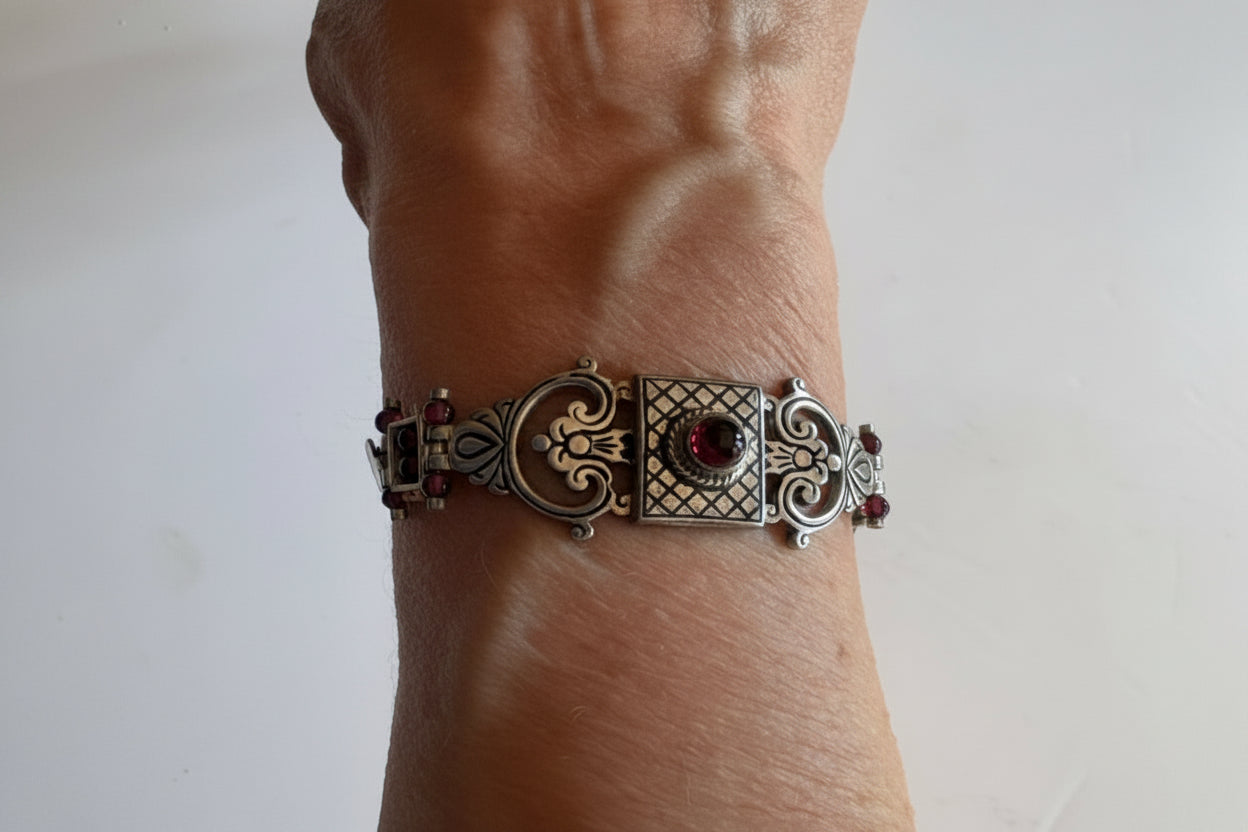 Decorative silver bracelet with red stones on a wrist against a plain background