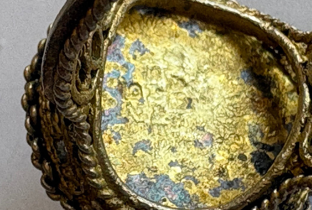 Close-up of an ornate gold earring with intricate designs on a white background