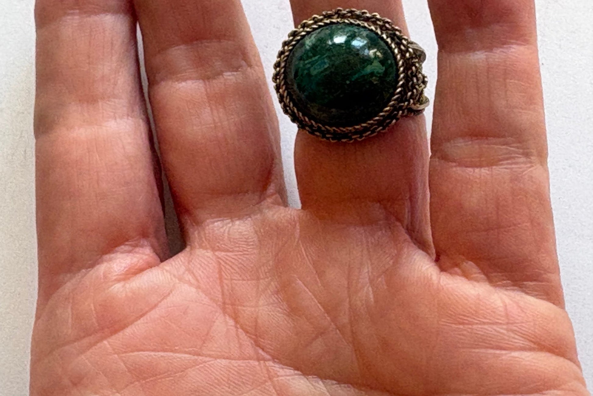 Hand wearing a ring with a green gemstone on a white background