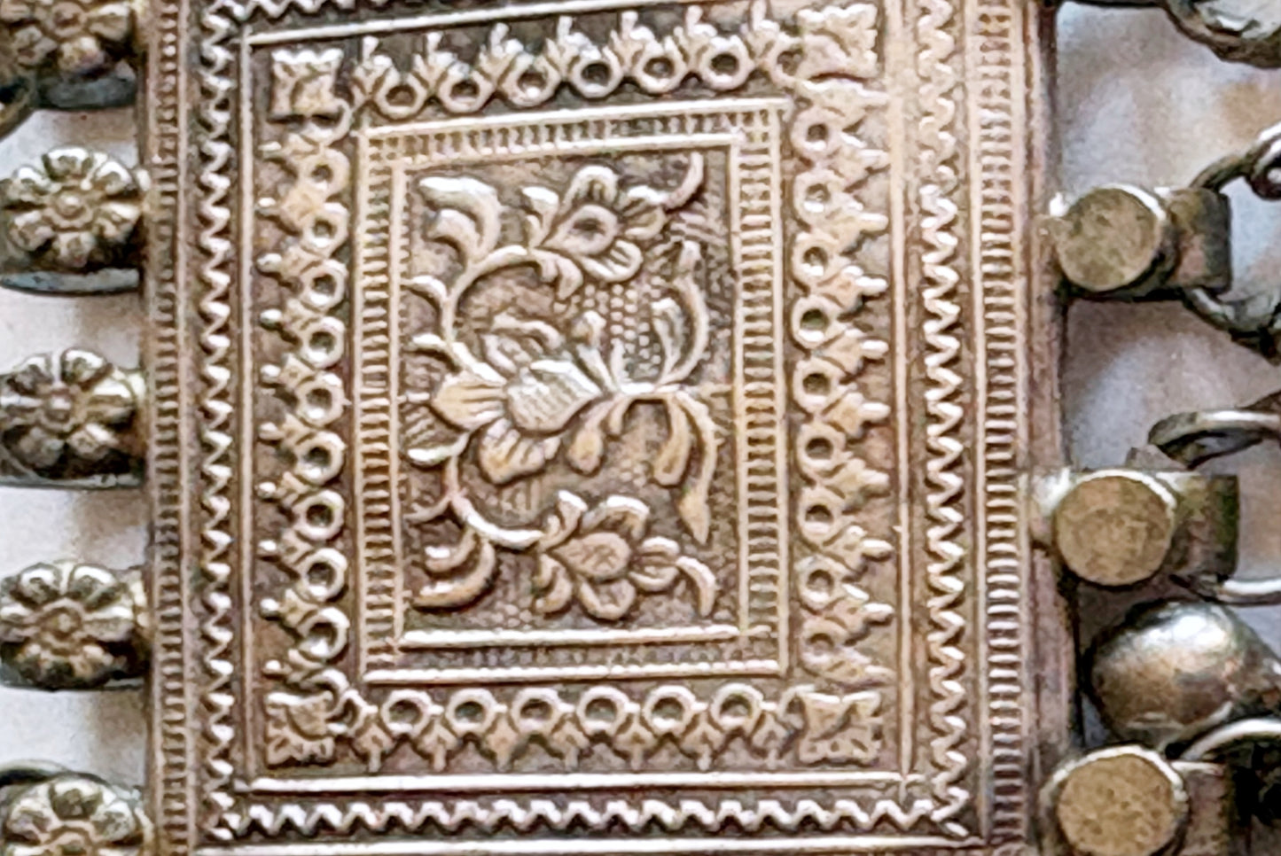Close-up of an ornate silver pendant with embossed floral and geometric patterns.