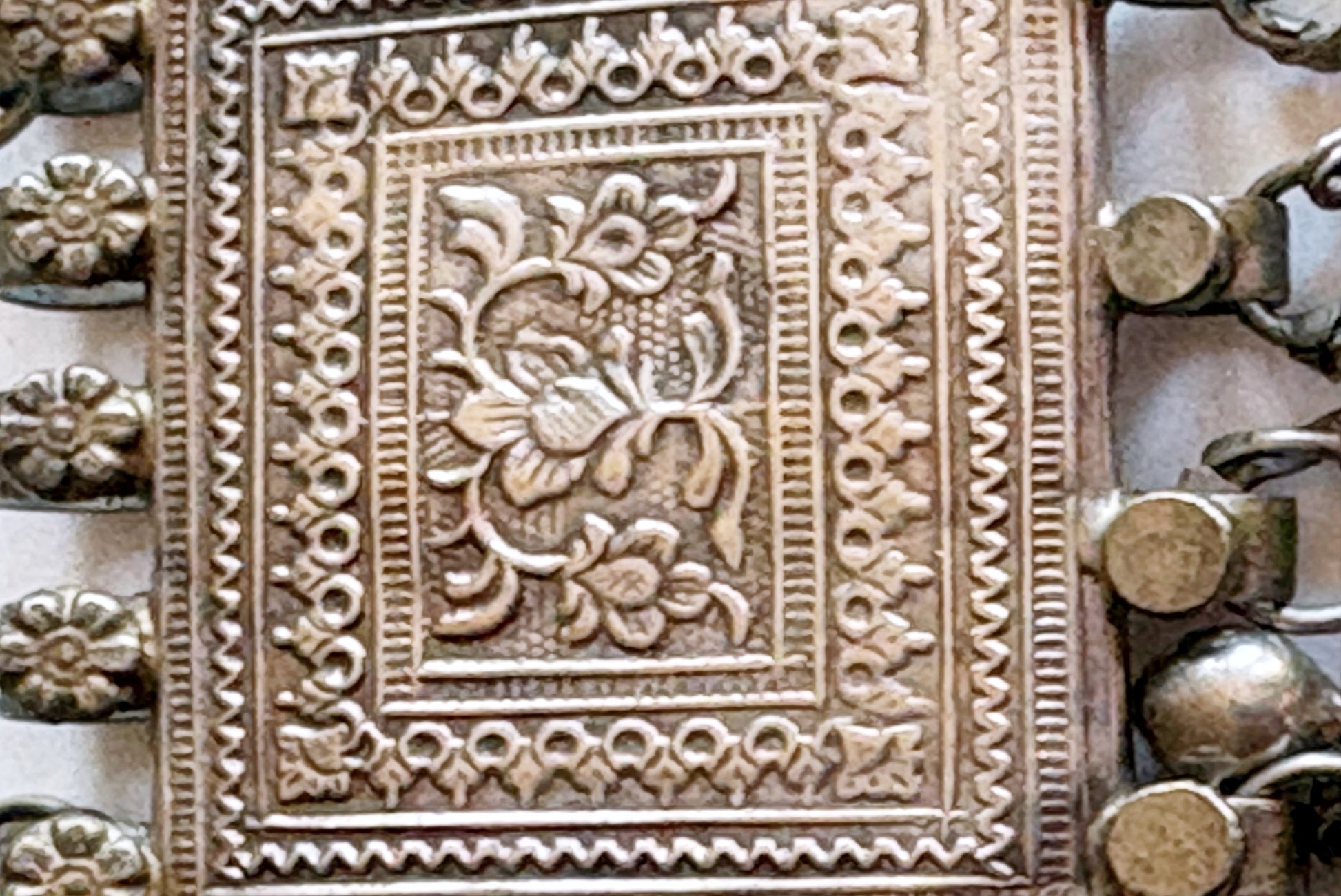 Close-up of an ornate silver pendant with embossed floral and geometric patterns.