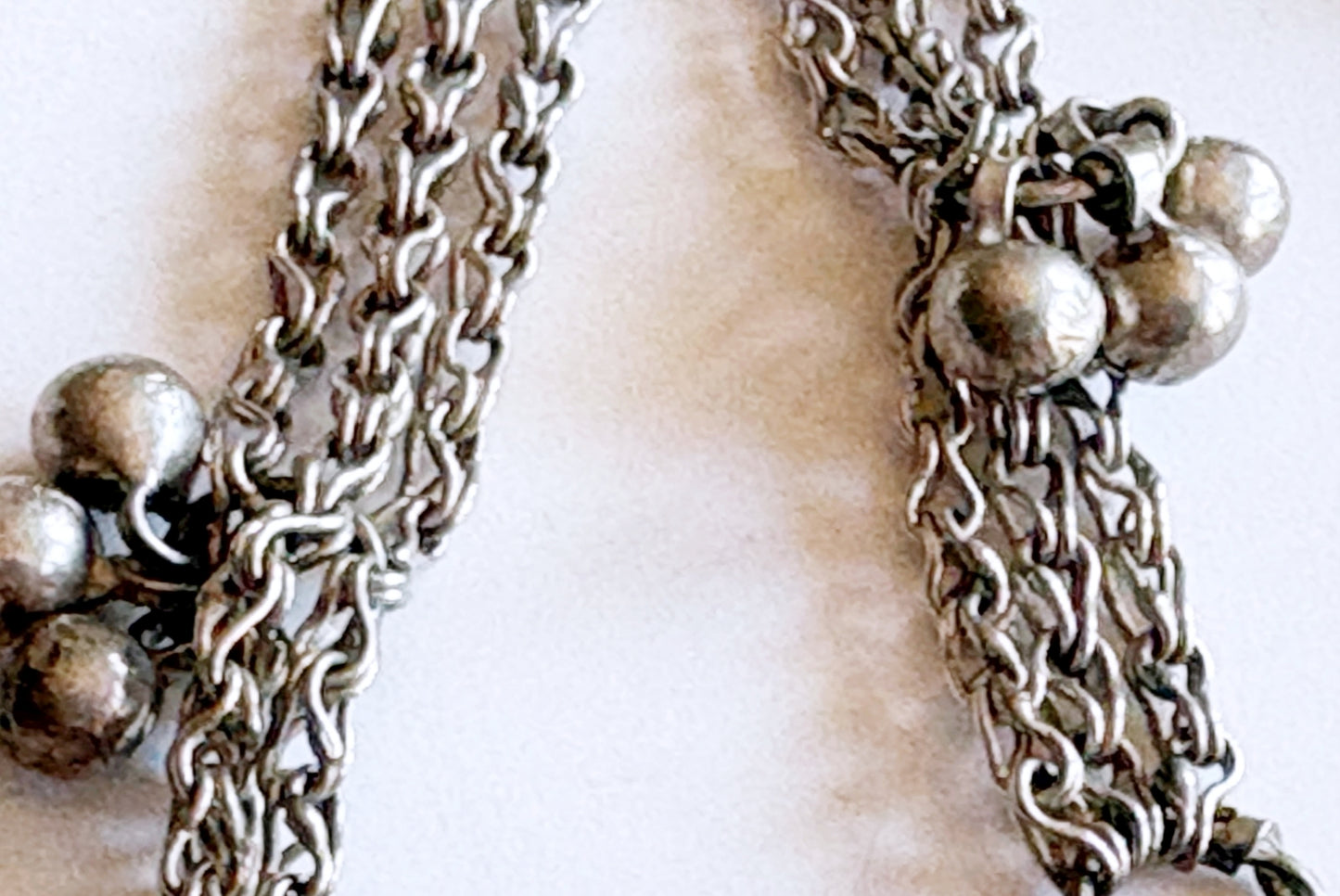 Close-up of a silver chain necklace with decorative bead clusters at the ends, shown against a light neutral background.