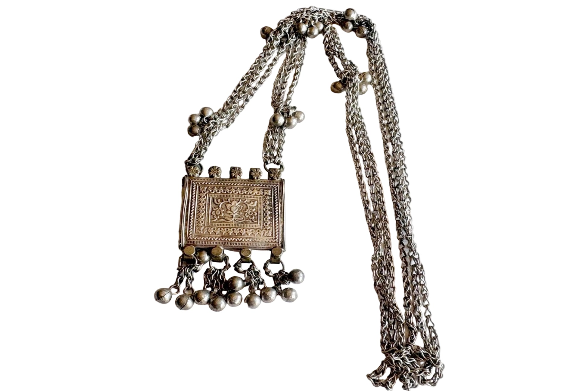 An silver necklace featuring a rectangular embossed pendant with dangling beaded chains and a long chain strap, displayed on a plain white background.
