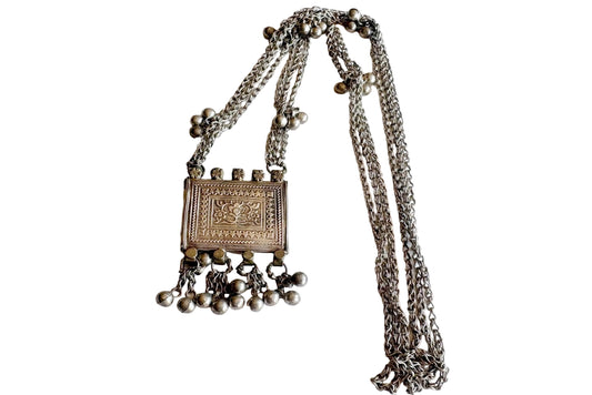 An silver necklace featuring a rectangular embossed pendant with dangling beaded chains and a long chain strap, displayed on a plain white background.