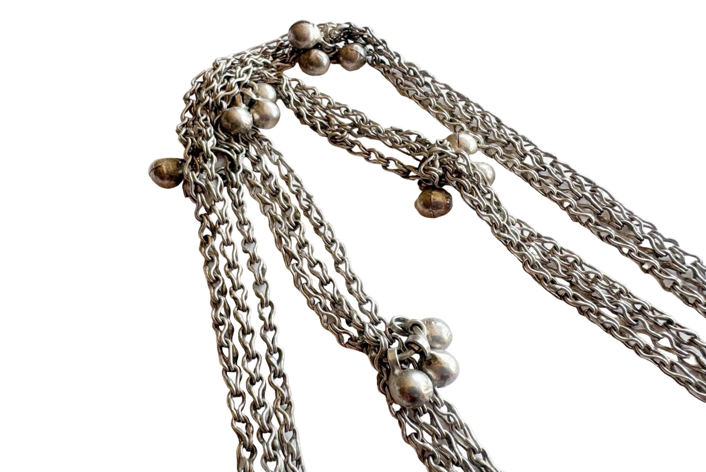 A close-up of a silver chain necklace with multiple draped chains and small silver bead details, photographed on a plain light background.