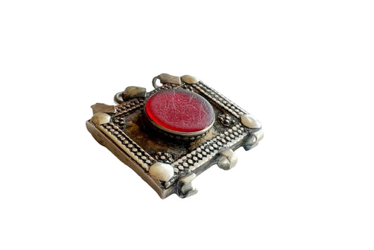 Decorative brooch with red center and metallic frame on a white background