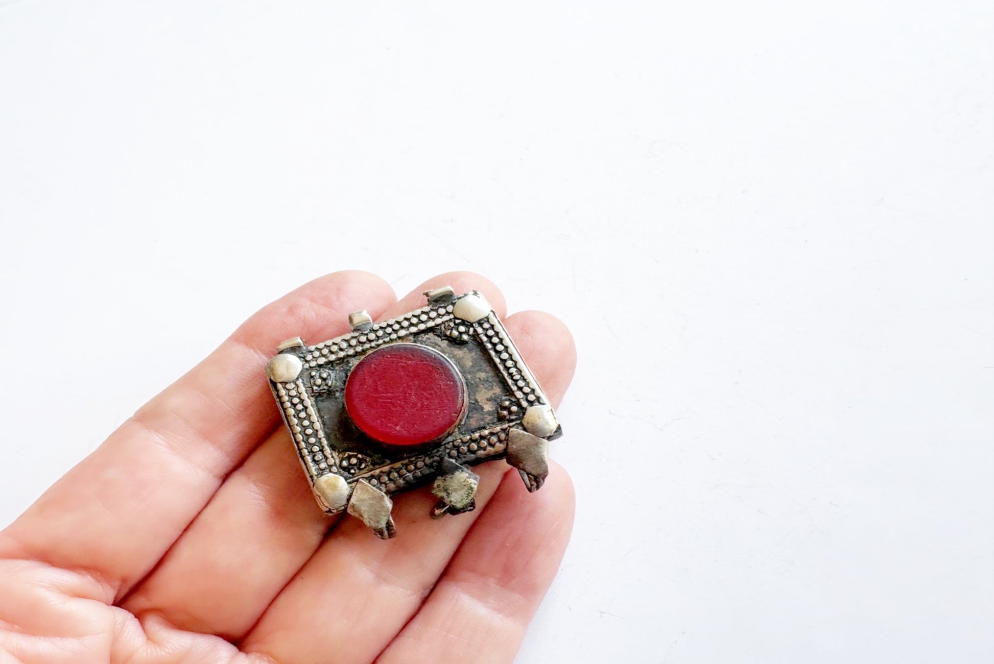 Hand holding a decorative pendant with a red stone on a white background