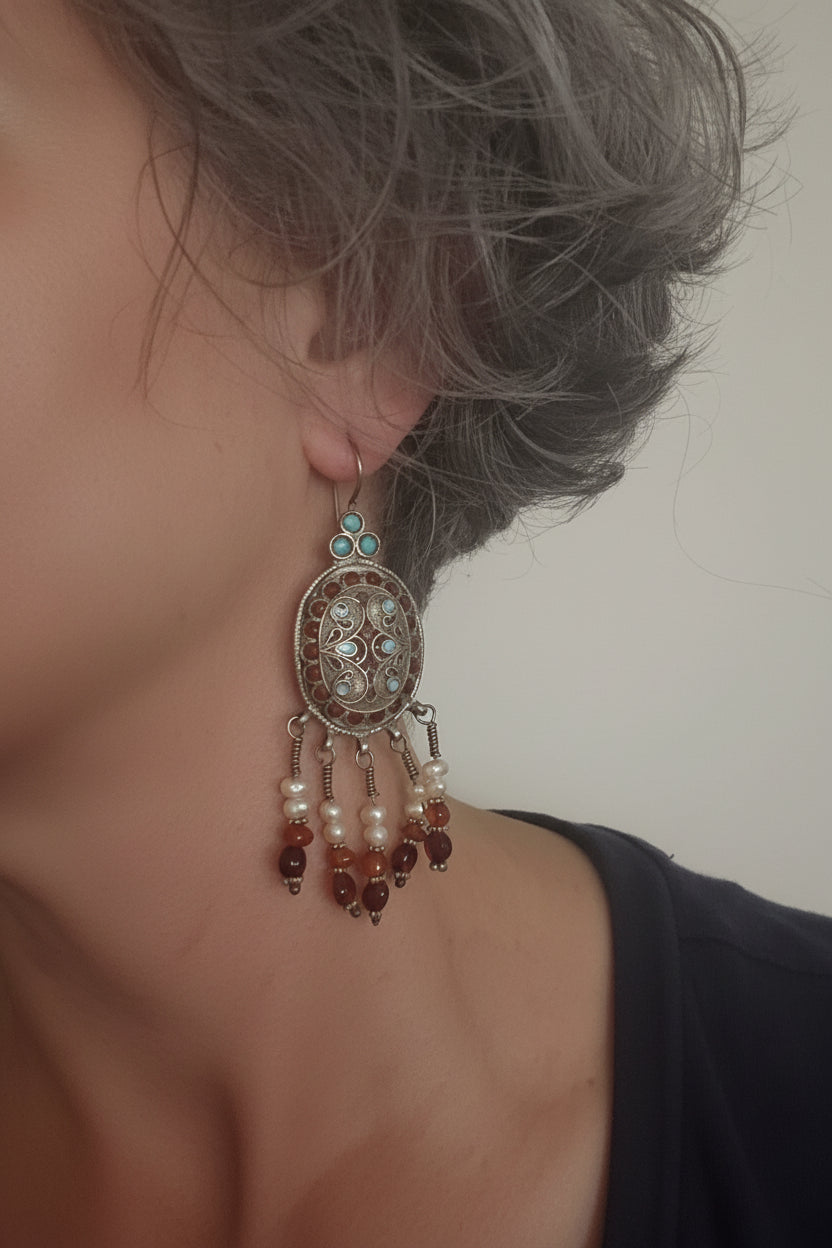 Close-up of an ornate earring with beads on a person's ear against a neutral background