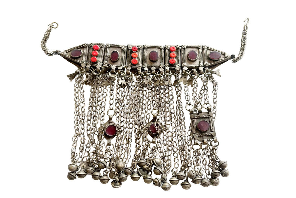 An ornate silver-toned traditional necklace with multiple dangling chains, small bell charms, and rectangular red glass accents, displayed against a plain white background.