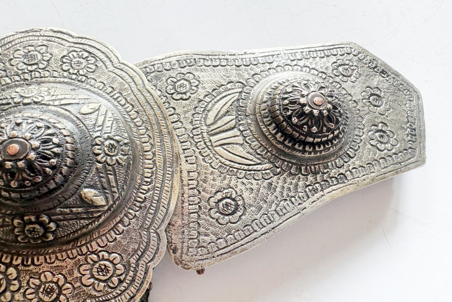 An ornate metal belt buckle with intricate floral engravings and raised central medallions, shown on a plain white background.