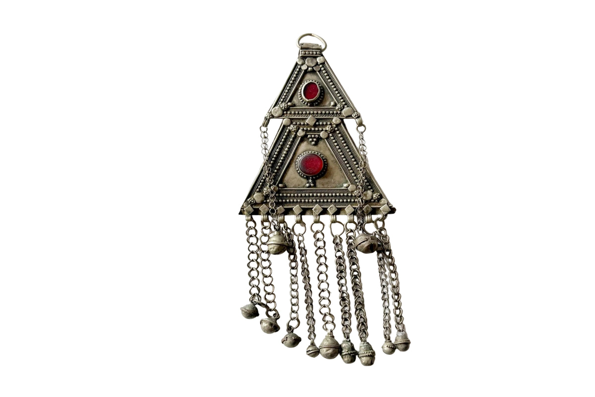 A silver-toned triangular pendant with red gemstone accents and dangling chain bells, photographed against a plain white background.