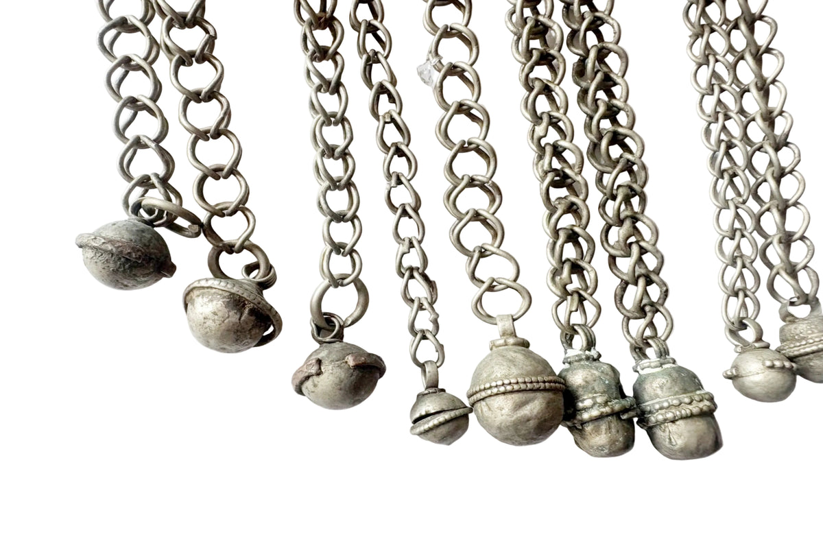A close-up of several silver-toned chains with small hanging bells, arranged side by side on a plain white background.