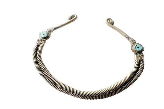 An antique-style silver-toned metal torc necklace with intricate woven detailing and small turquoise stone accents on both ends, displayed on a clean white background.