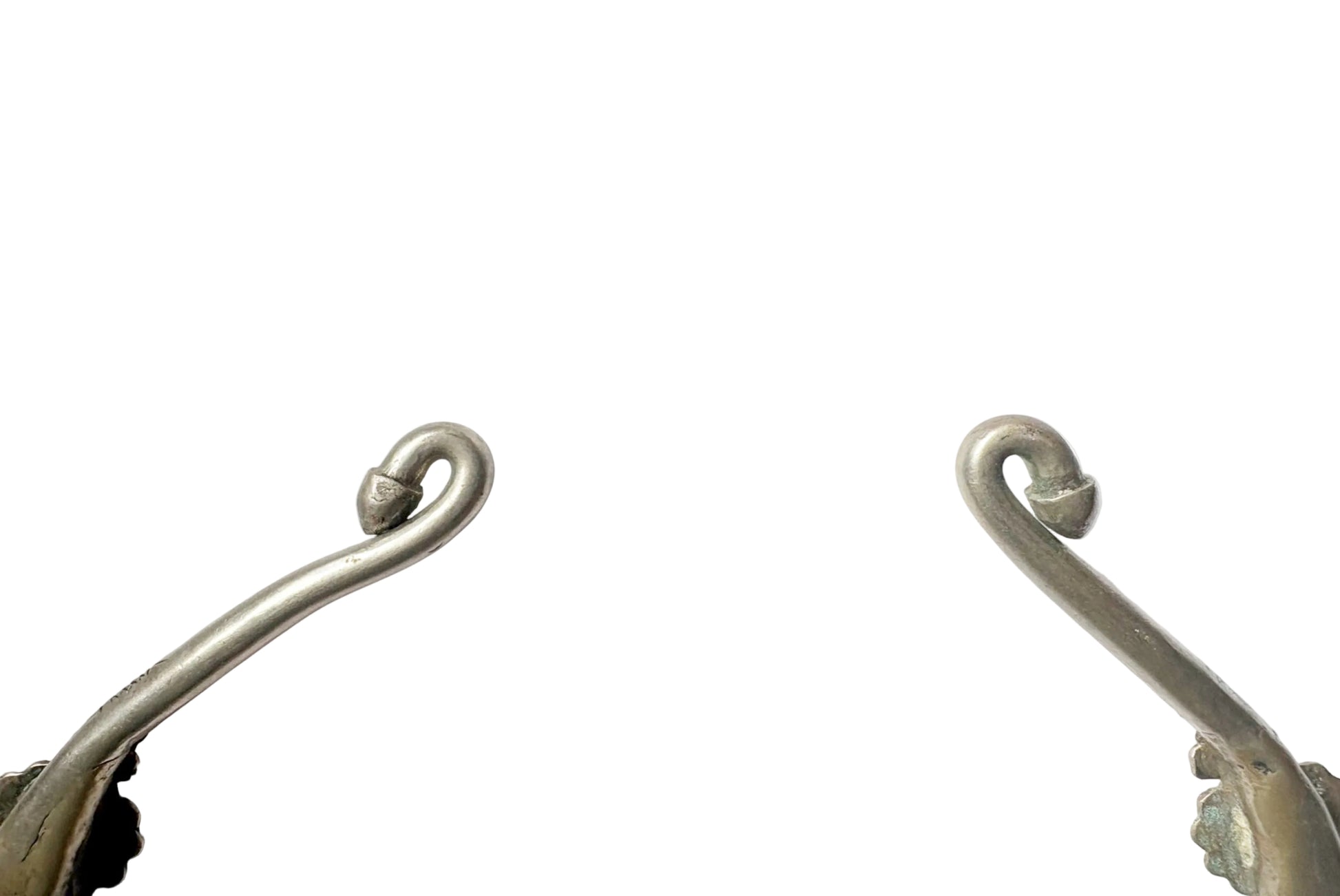 A close-up of the two curved finials of a torc necklace on either side of a plain white background.