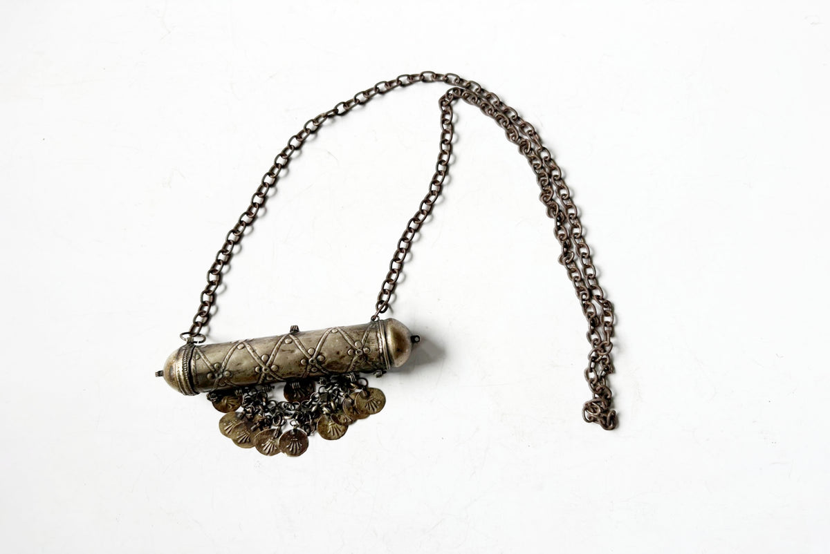 An antique-style metal pendant necklace featuring a cylindrical, textured centerpiece with dangling coin-like charms, suspended from a dark chain on a white background.