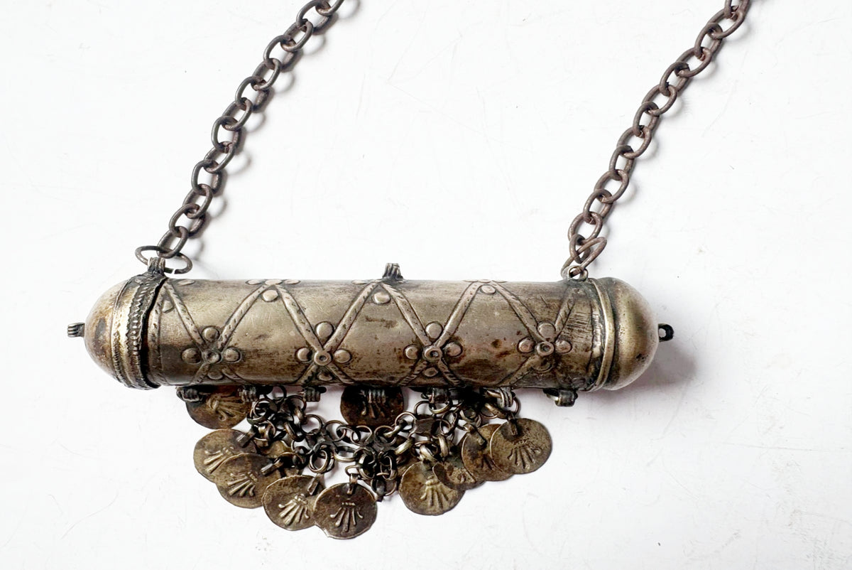 An antique-style silver-toned metal pendant necklace featuring a cylindrical barrel-shaped centerpiece with engraved diamond patterns, hanging coin charms, and a chain necklace on a white background.