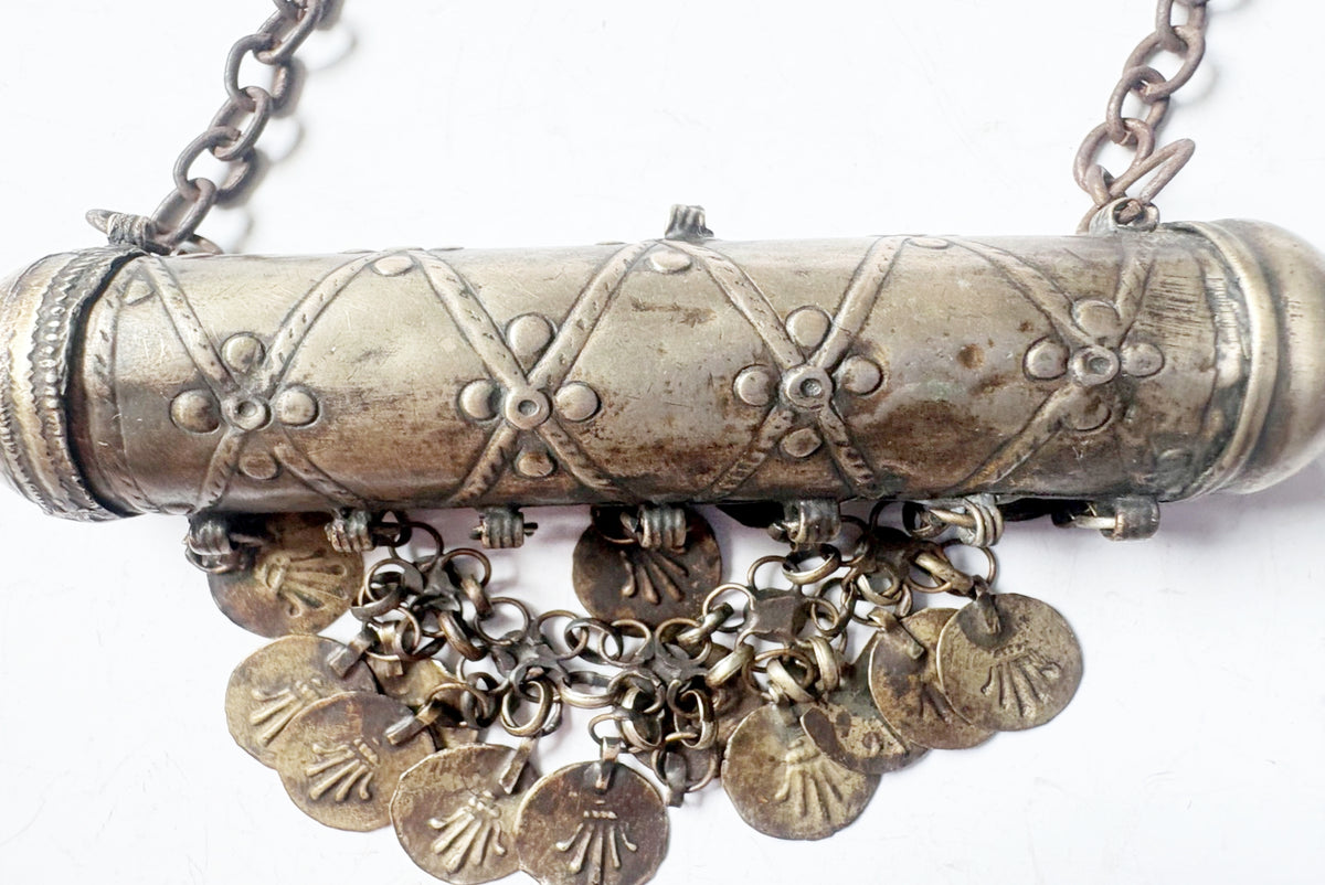 An antique-style silver-toned cylindrical pendant necklace with decorative crisscross engravings, a top chain, and multiple dangling coin-shaped charms on a white background.