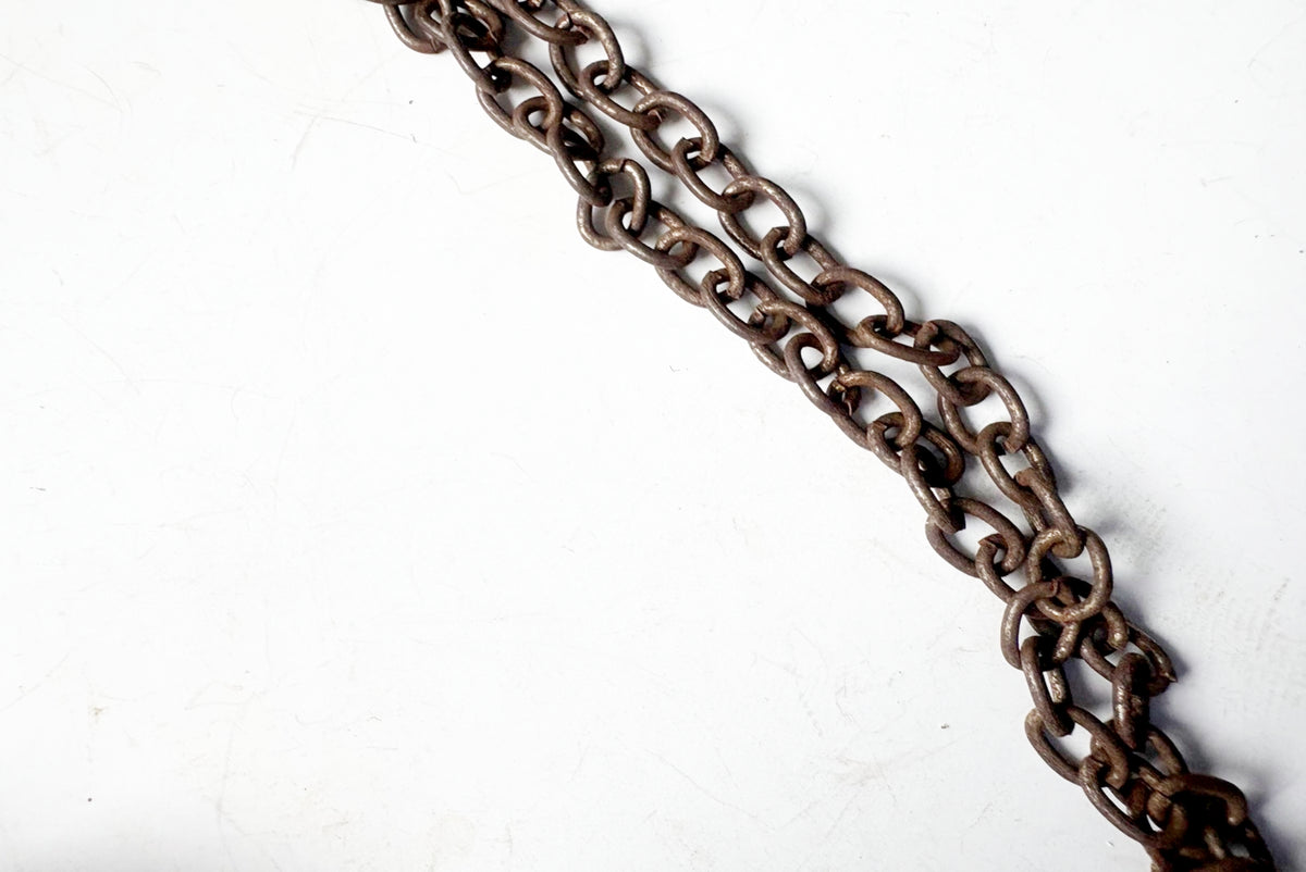 A close-up of a dark, weathered metal chain running diagonally across a plain white background.