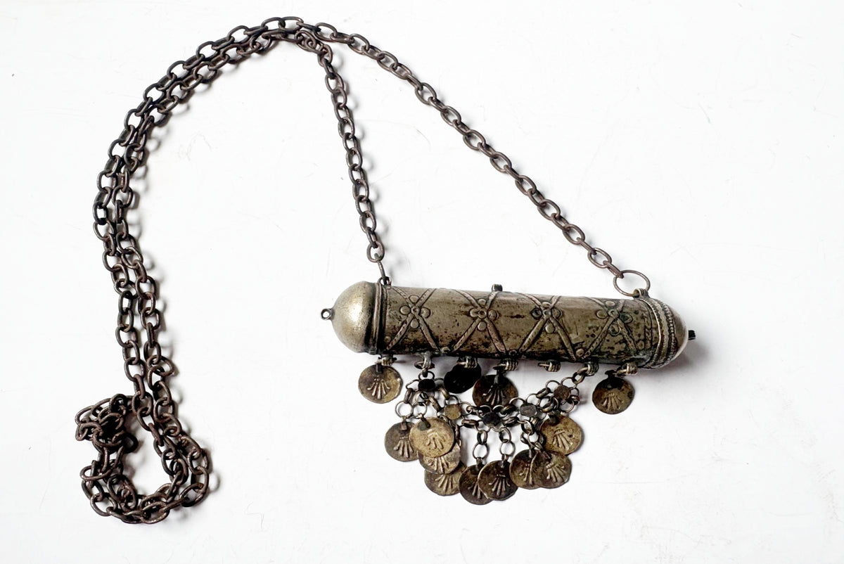An antique-style metal belly chain necklace featuring a cylindrical pendant with geometric wirework detailing, a metallic cap, and multiple dangling coin charms, shown on a plain white background.