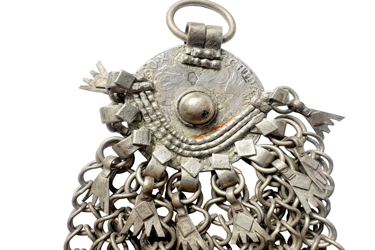 An antique silver coin pendant with a circular disc, central bead and multiple dangling chain fringes on a white background.