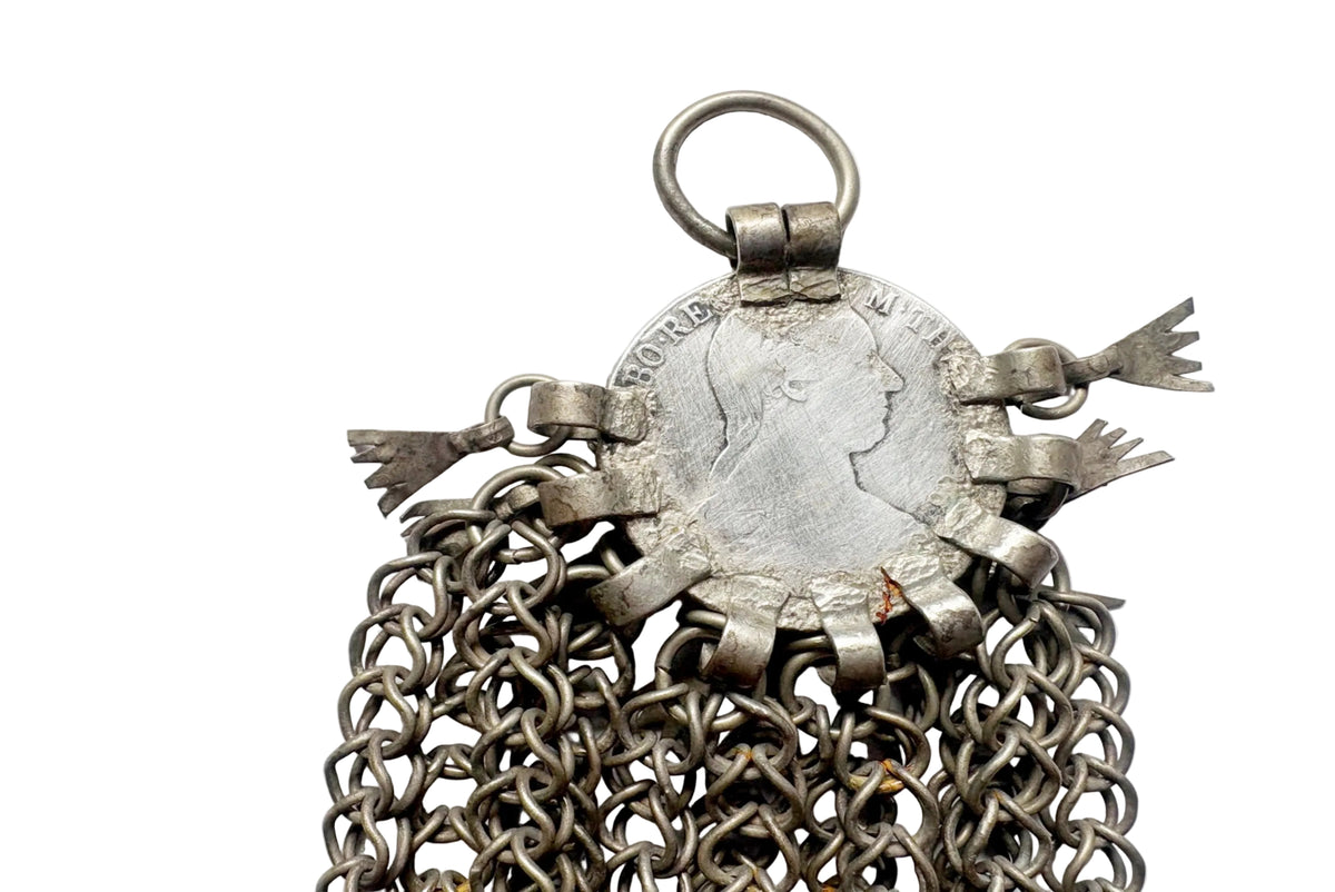 An antique silver Maria Theresa coin pendant with chainmail  chains and decorative metal lozenges, shown on a white background.