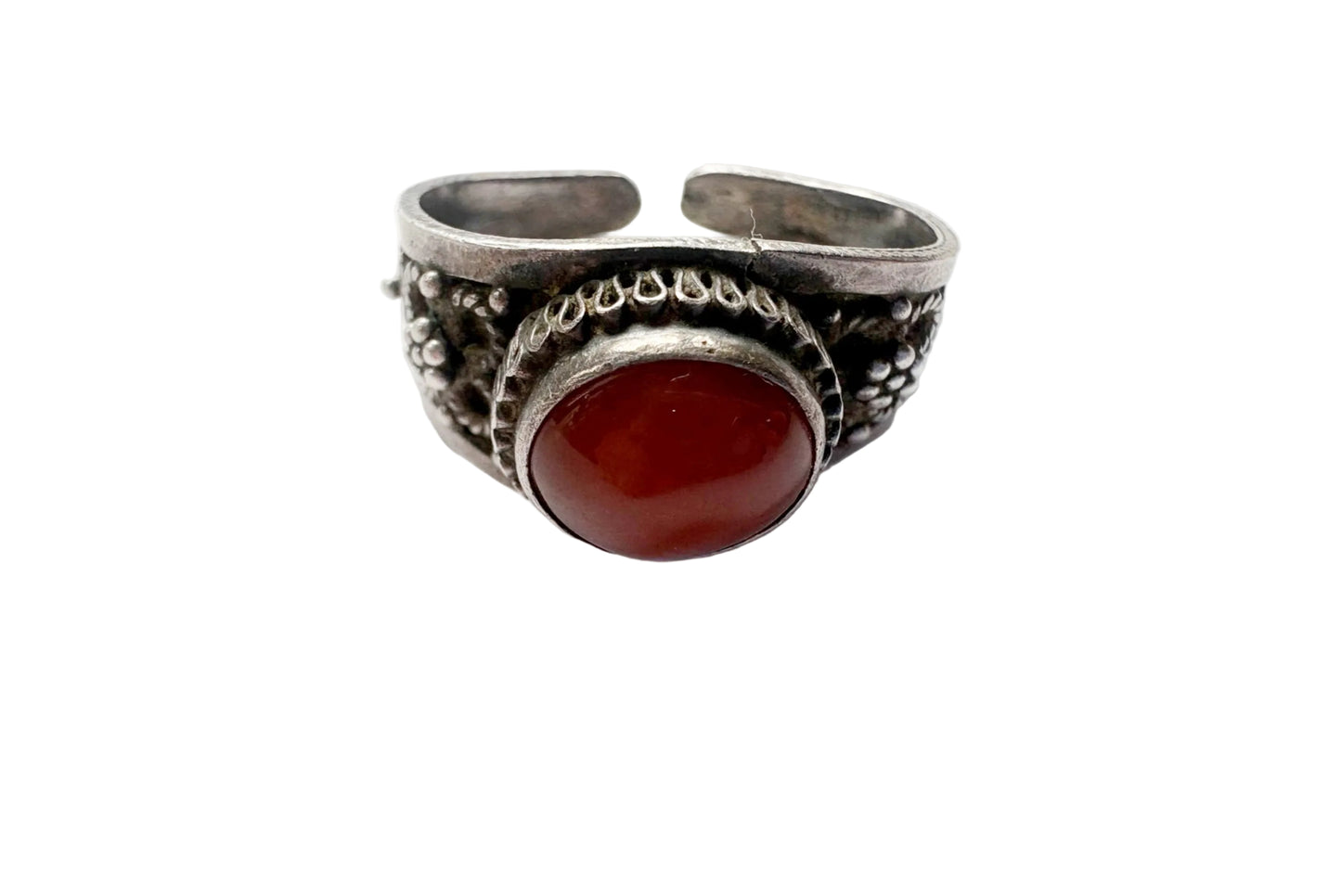 A silver open band ring with ornate filigree detailing and a large oval red cabochon stone, shown on a plain white surface.