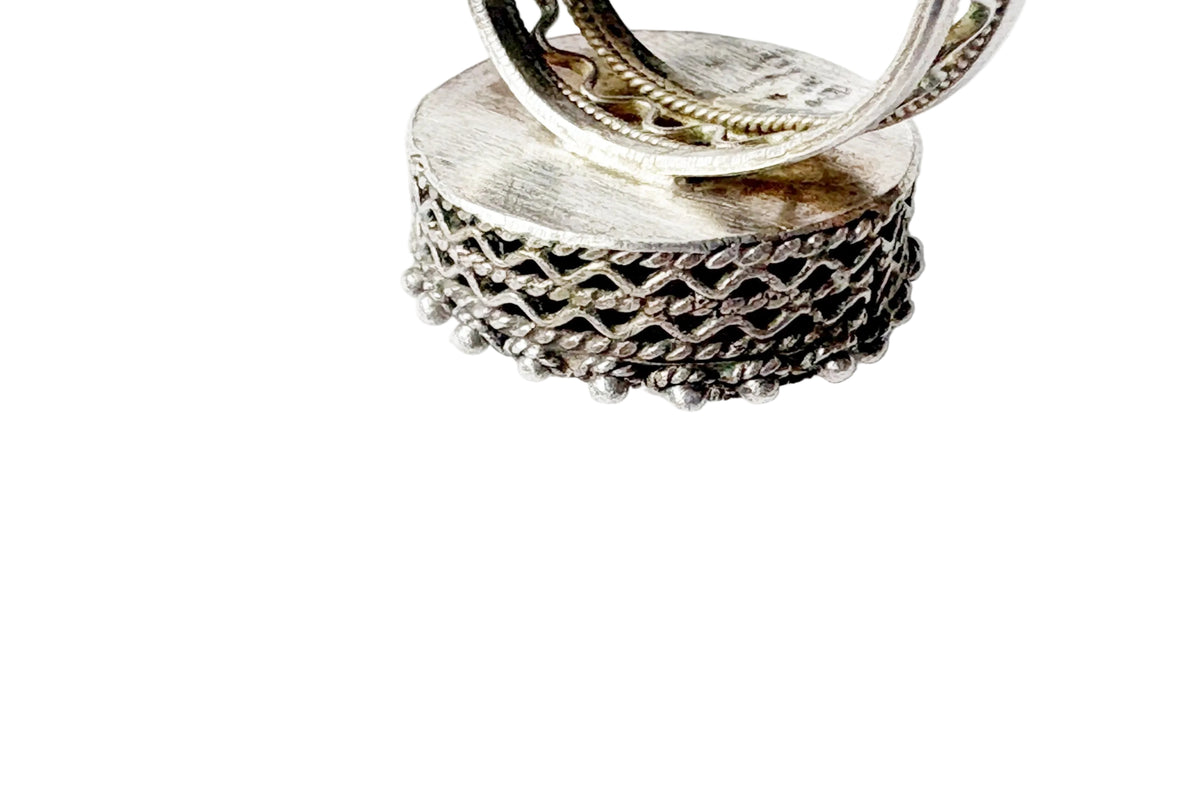 A close-up of a silver ring featuring a textured, woven basket-like band, shown against a plain white background.
