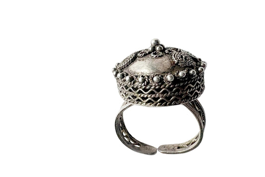 An vintage silver ring with an intricate filigree crown-like top and an adjustable band, photographed on a light white background.