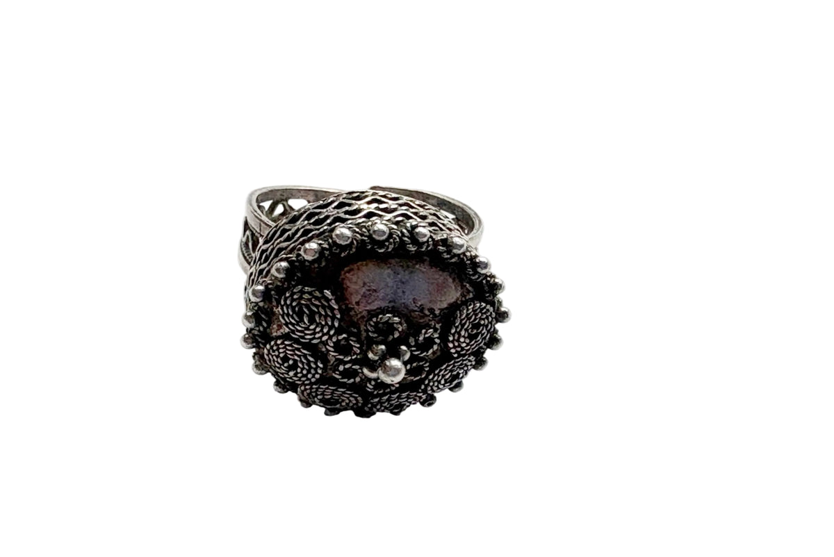 An ornate silver ring surrounded by intricate filigree and small bead details, set against a plain white background.