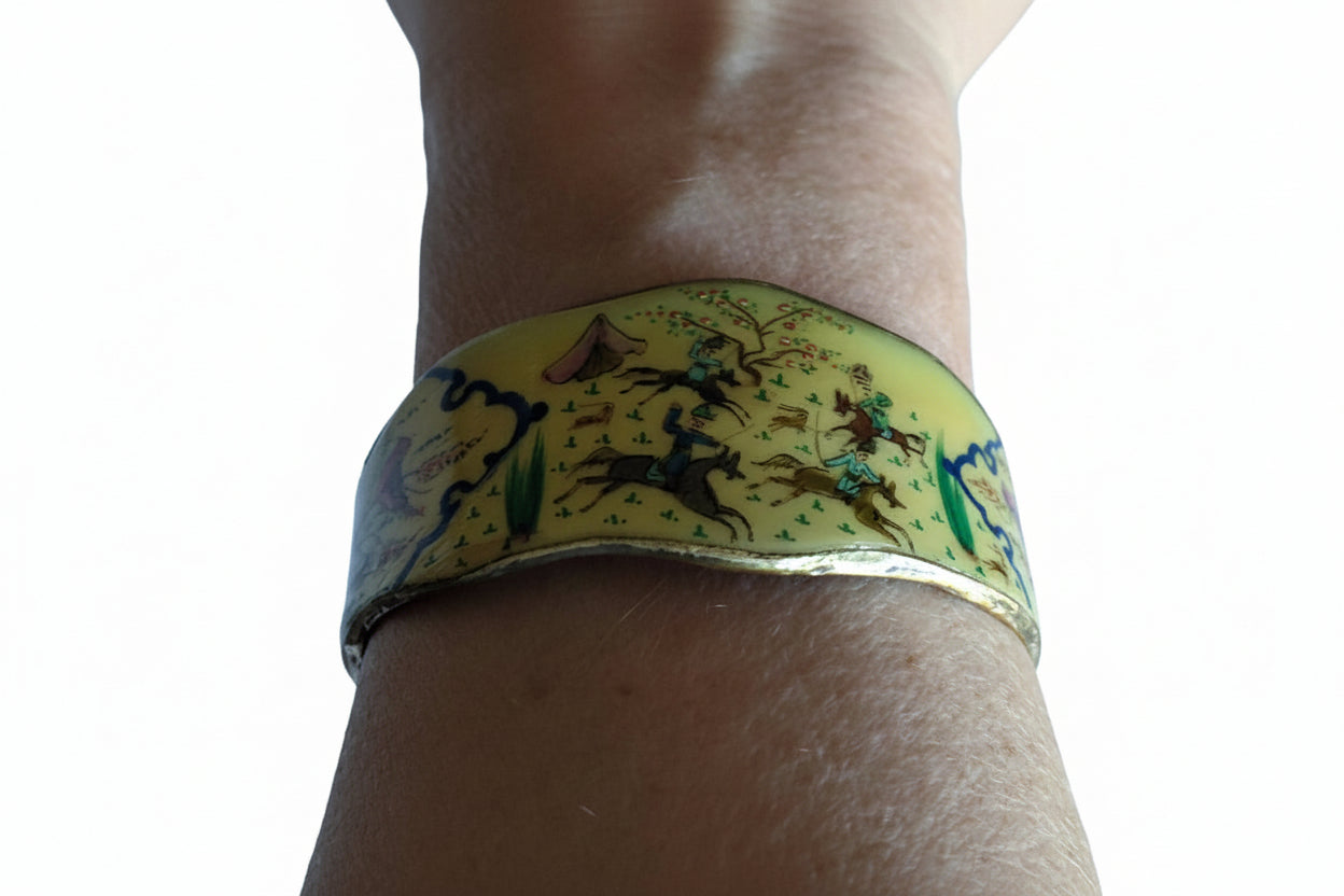 Yellow cuff bracelet with animal designs on a wrist against a clear blue sky.