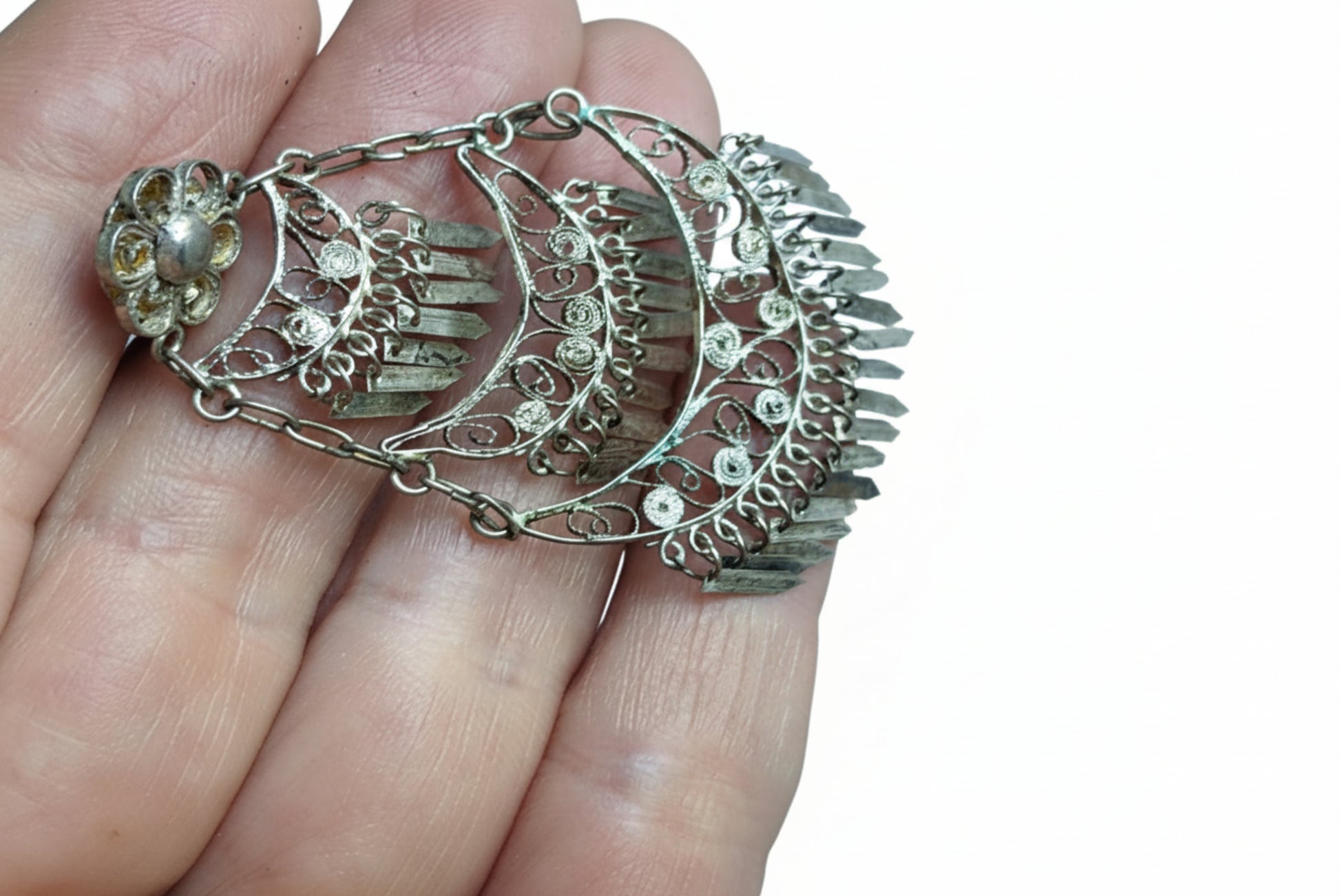 Filigree silver earrings held in a hand against a white background