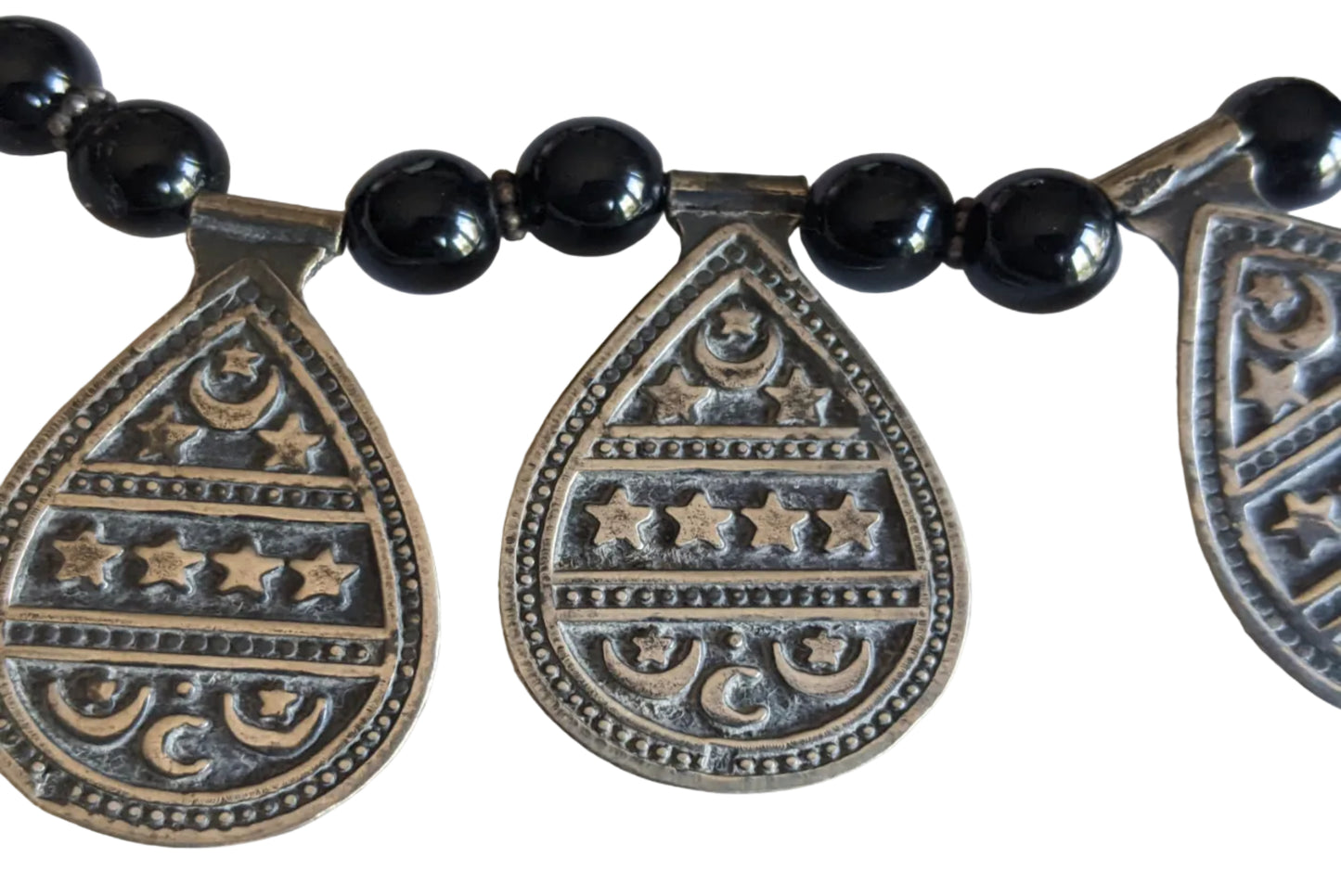 Necklace with black beads and silver teardrop-shaped pendants on a white background