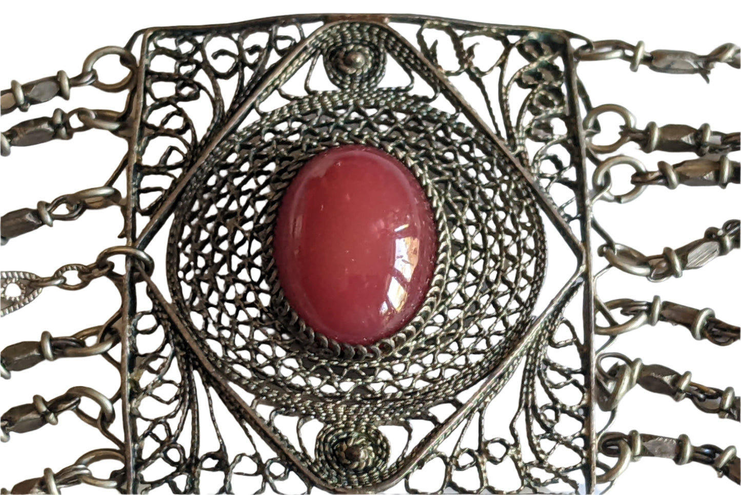 Decorative brooch with red gemstone and intricate metalwork on a white background