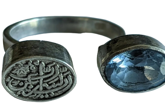Silver ring with engraved design and blue gemstone on a white background
