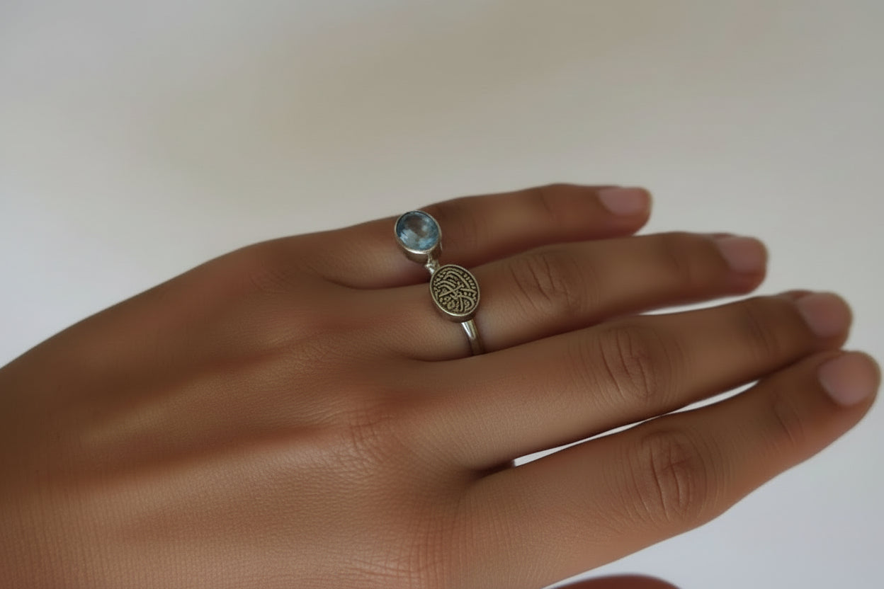 Ring with a blue topaz gemstone on a person's finger against a neutral background