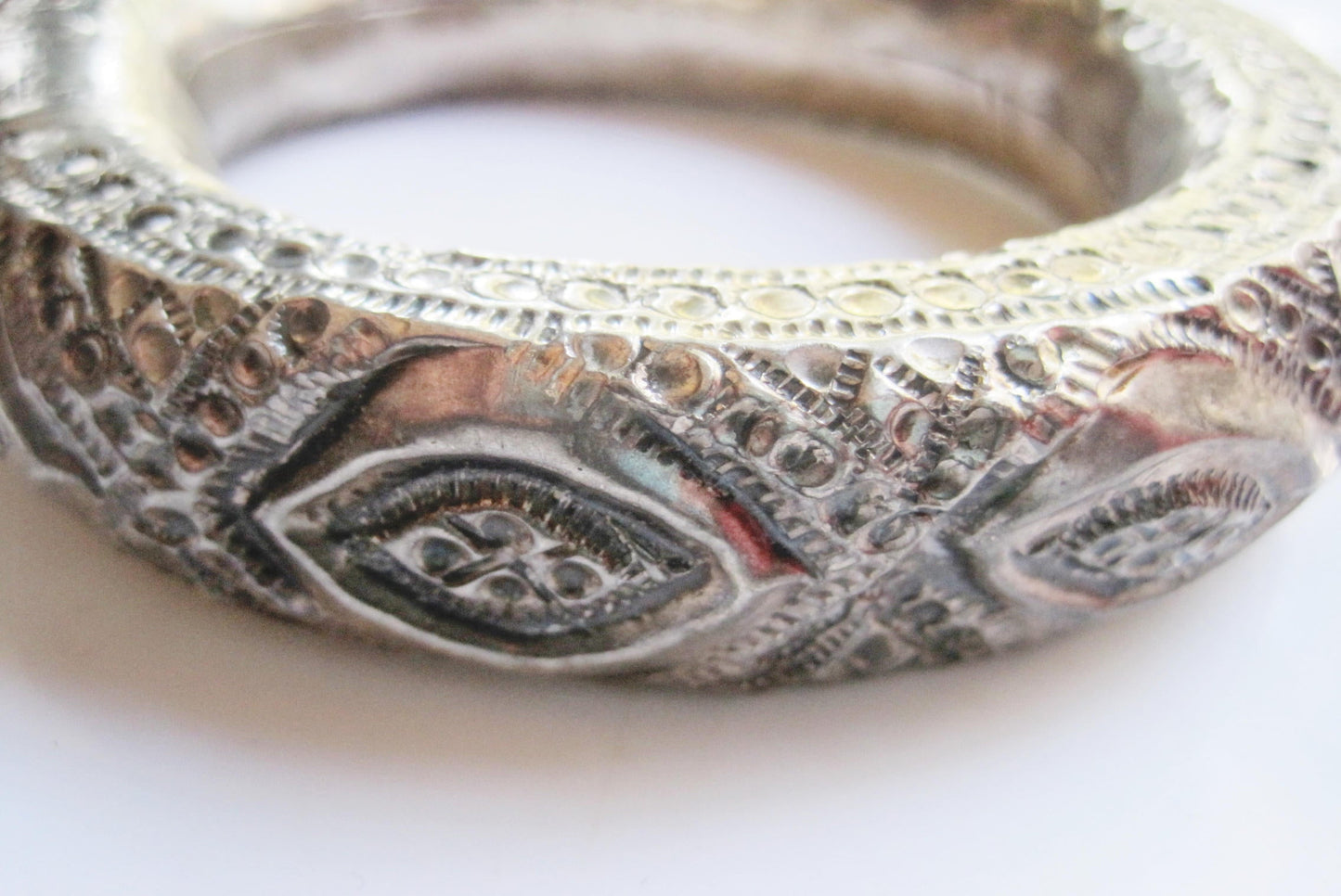 A close-up of a textured silver bangle featuring raised eye-like motifs and intricate hammered details, set against a plain white background.
