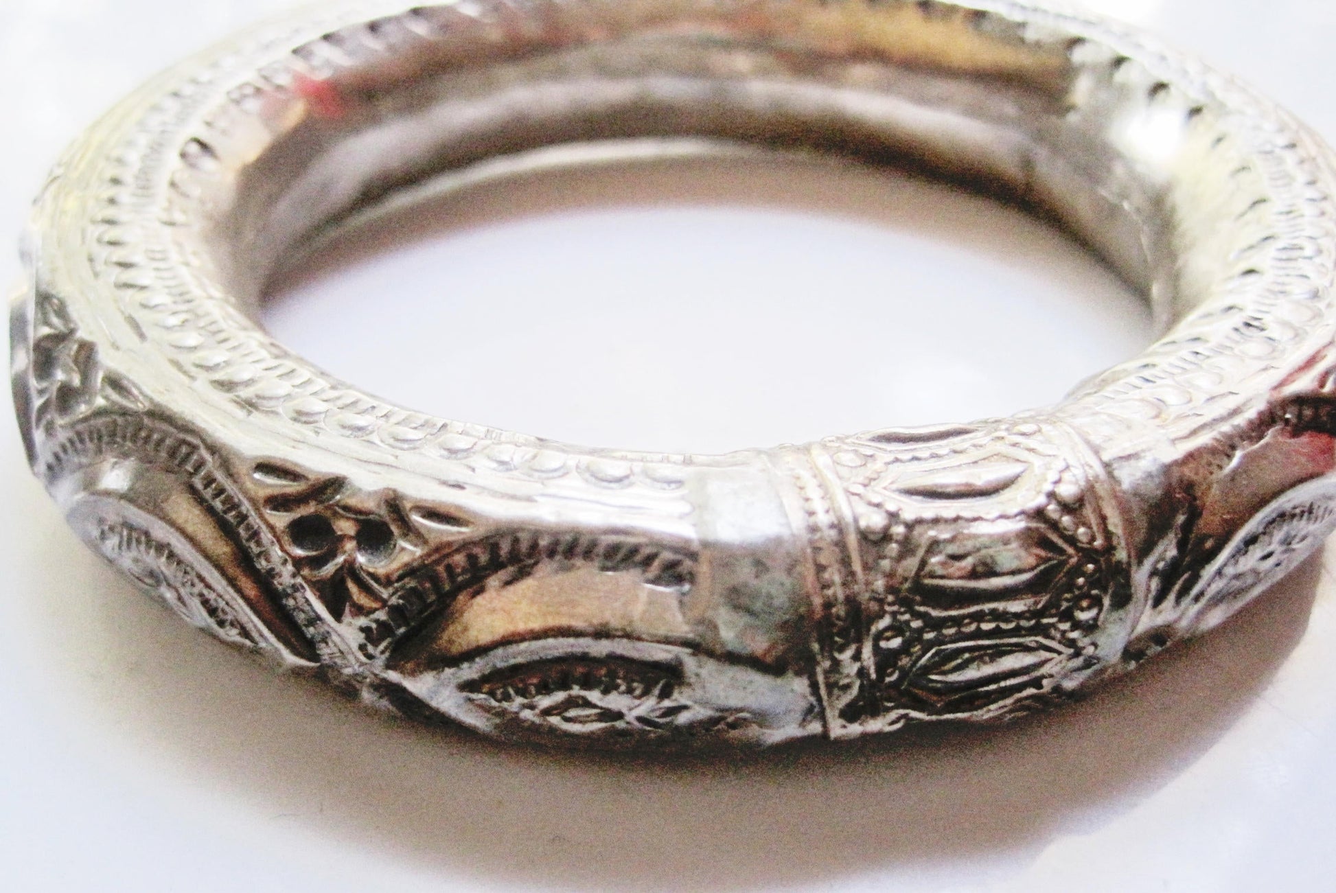 An ornate silver bangle bracelet with intricate engraved patterns and filigree details, shown on a plain light background.