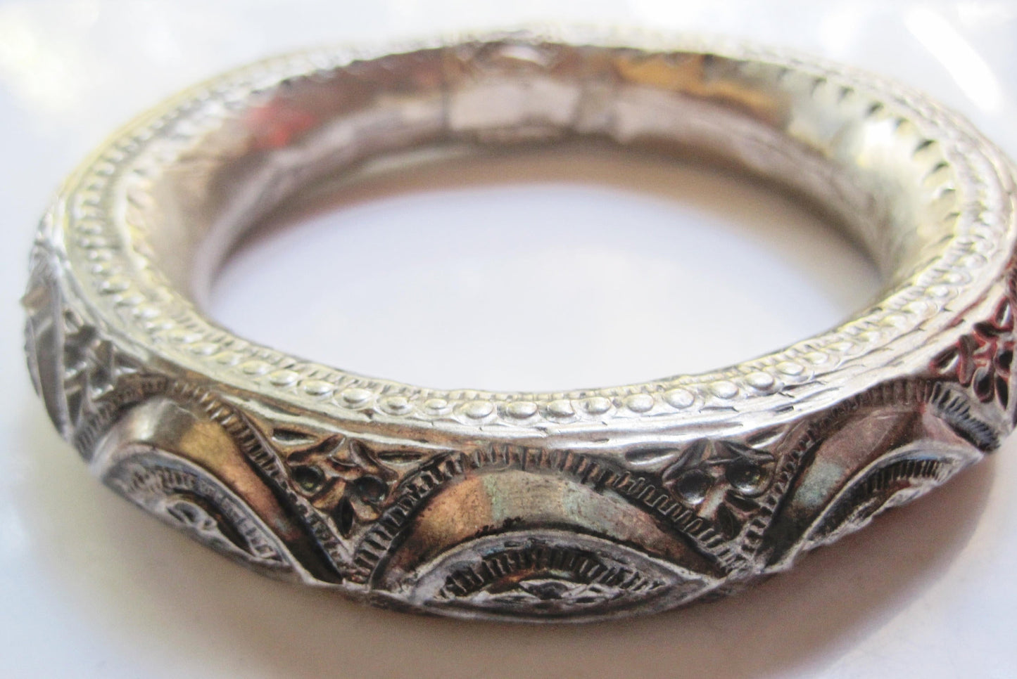 An ornate silver bracelet with intricate filigree and floral engravings, photographed close-up on a light background.