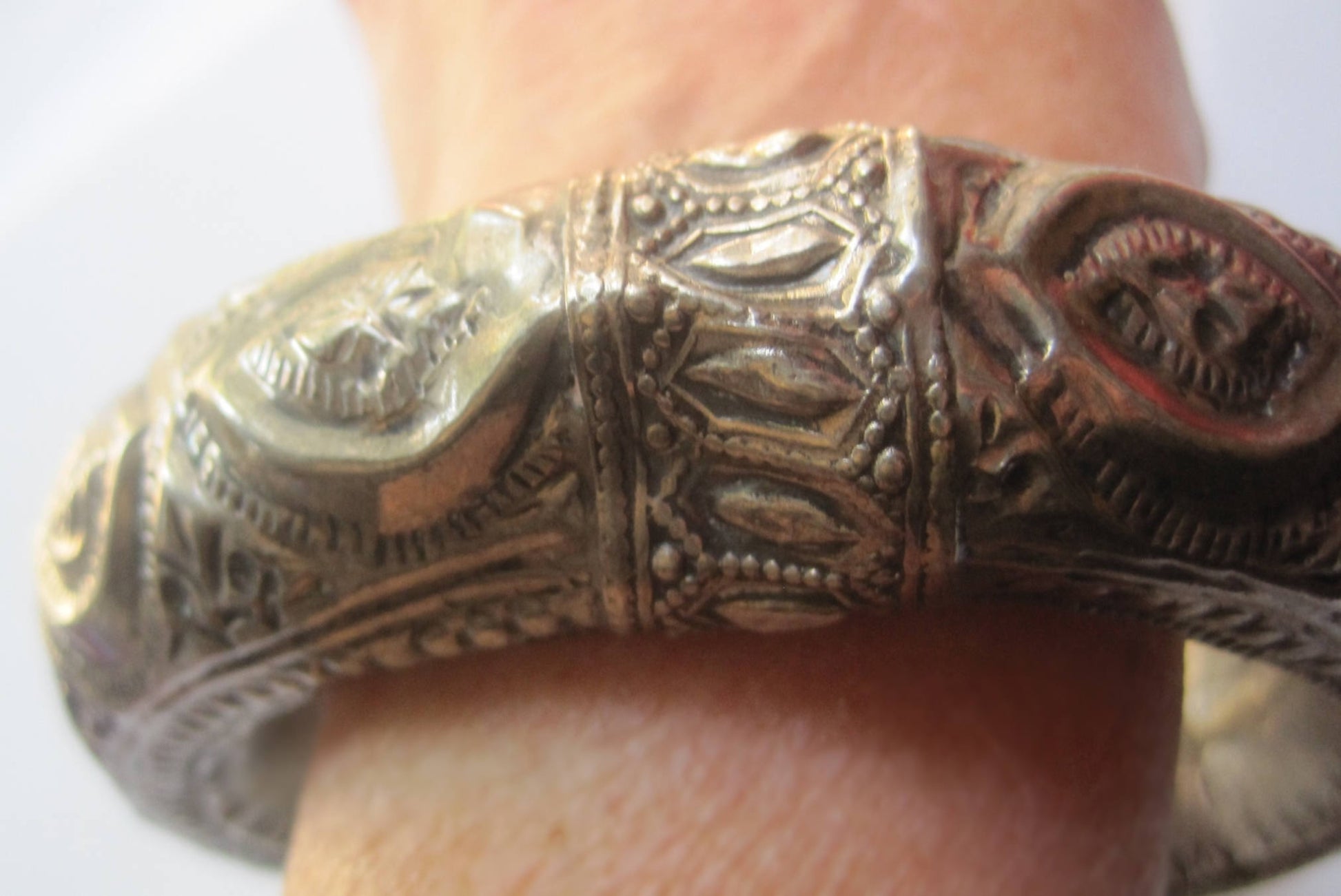 An ornate silver bangle bracelet with intricate engraved patterns, shown worn on a person's wrist.